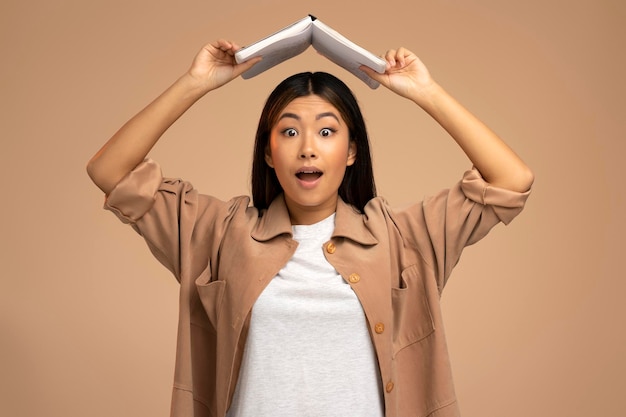 Portrait of positive woman standing holding book over head studying and education