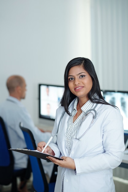 Photo portrait of positive young female physician taking notes in document after having online meeting with colleagues from other clinics