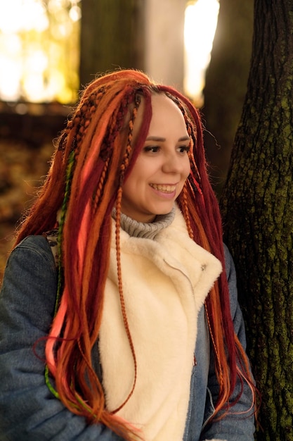 Portrait of positive young woman with dreadlocks in forest park Pretty female with bright hairstyle looking away smiling