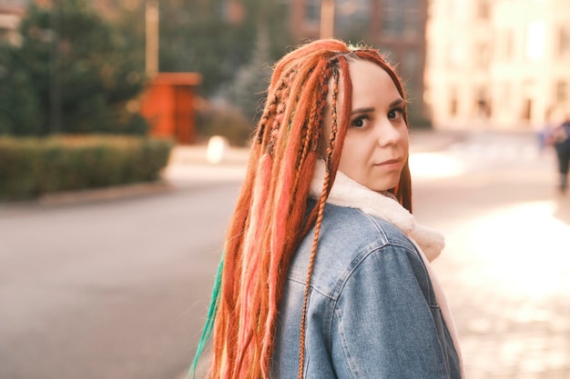 Portrait of positive young woman with dreadlocks on modern city street Pretty female with bright hairstyle looking away smiling