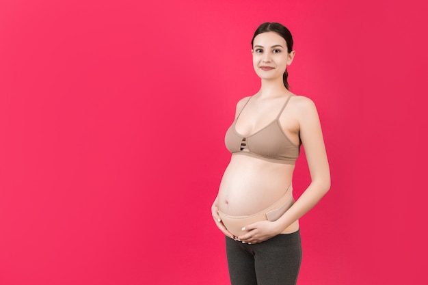 Portrait of pregnancy bandage dressed on pregnant woman for reducing backpain at pink surface with copy space