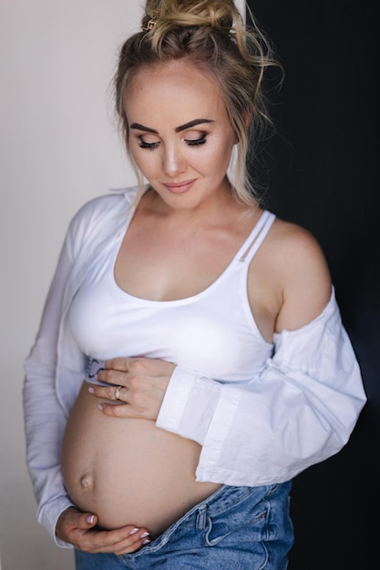 Portrait of pregnant woman in studio denim style beautiful future mother put her her hands on her