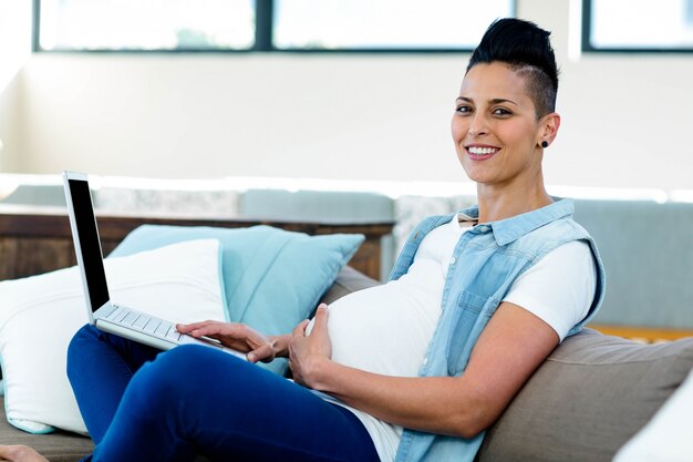 Portrait of pregnant woman using laptop while relaxing on sofa in living room