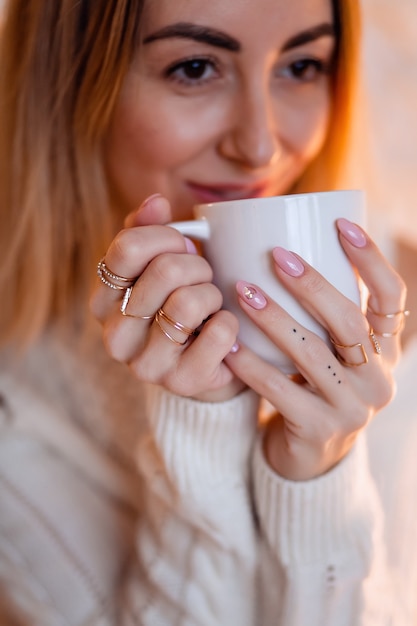 Portrait of a pretty blonde in a cozy home sweater with cup