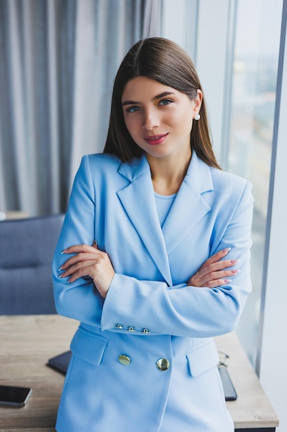 Portrait of a pretty brunette in a blue jacket in the office near the panoramic window with a view of the city Happy business woman in the office