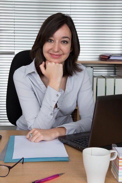 Portrait of a pretty businesswoman at the office with her hand to her chin looking into the camera