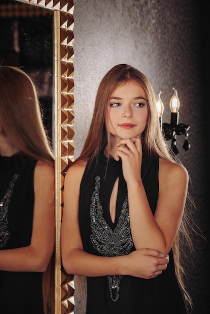 Portrait of pretty cute teenager girl in an elegant dress at mirror