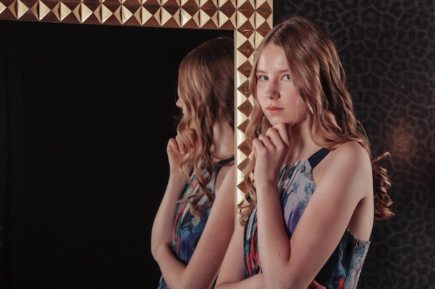 Portrait of pretty cute teenager girl in an elegant dress at mirror