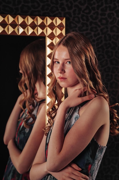 Portrait of pretty cute teenager girl in an elegant dress at mirror