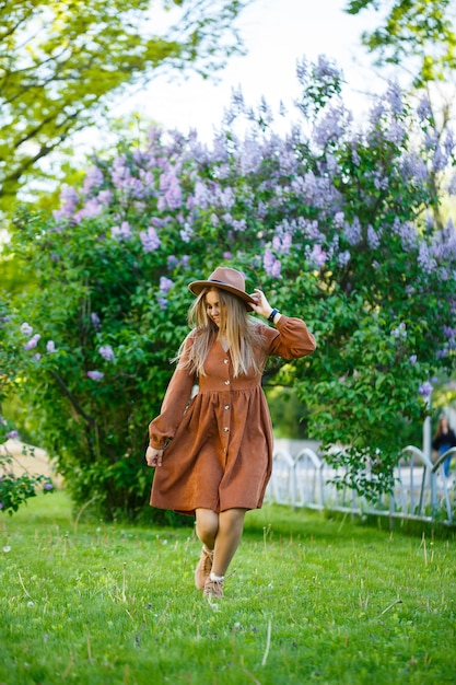 Portrait of a pretty girl in a brown hat with a lilac in the garden