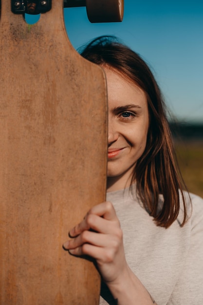 Portrait of a pretty girl holding a longboard in front of her face