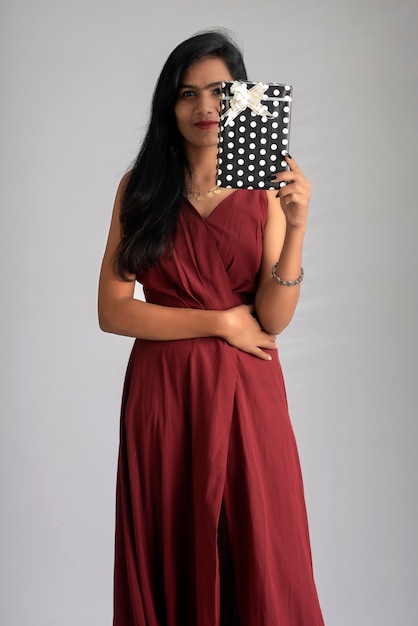 Portrait of a pretty girl holding and posing with gift box on grey background