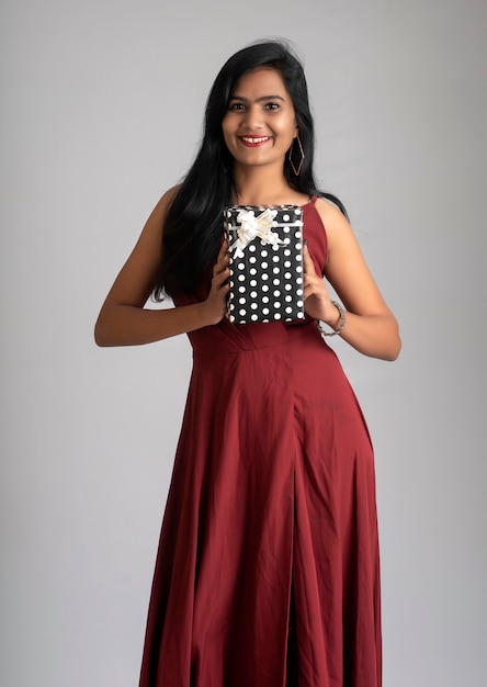 Portrait of a pretty girl holding and posing with gift box on grey background