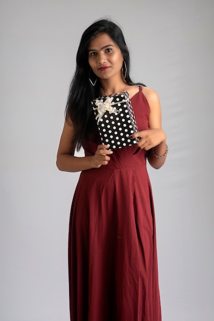 Portrait of a pretty girl holding and posing with gift box on grey background