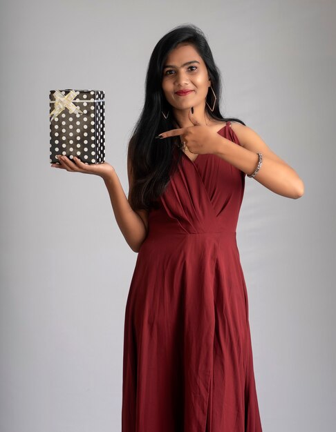 Portrait of a pretty girl holding and posing with gift box on grey background