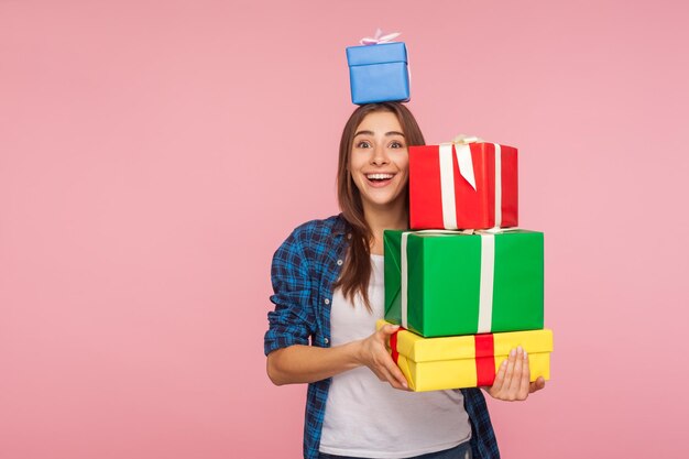 Portrait of pretty girl looking at camera with expression of sincere childhood happiness and holding many gifts one box on head enjoying birthday presents christmas holidays studio shot isolated