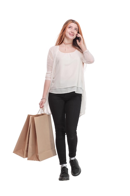 Portrait of a pretty happy girl talking on mobile phone while holding shopping bags and looking away