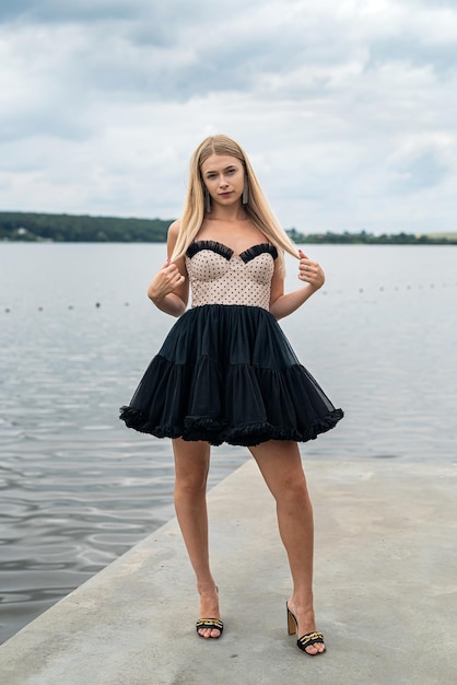 Portrait of pretty lady in fashionable dark dress near pond summer time