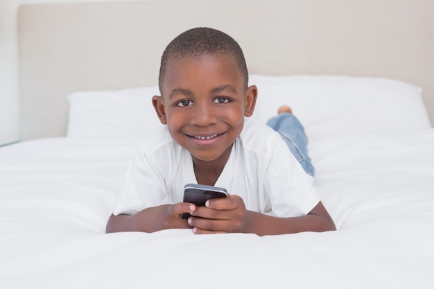 Portrait of a pretty little boy using smartphone in bed 