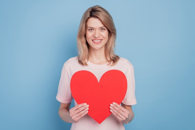 Portrait of pretty lovely sweet girl hands hold red paper heart figure card on blue background