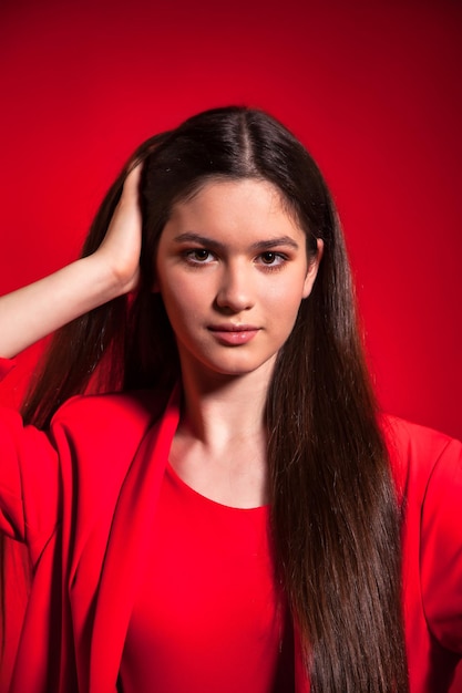 Portrait pretty positive teen girl in stylish red costume over red background looking at camera