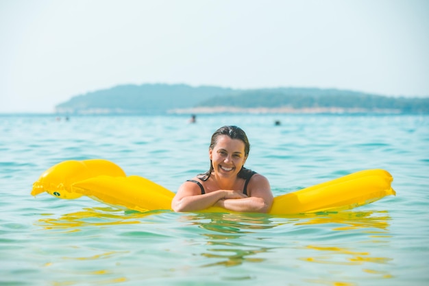 Portrait of pretty smiling woman on yellow inflatable mattress