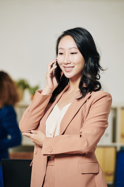 Portrait of pretty successful young female entrepreneur talking on phone with colleague