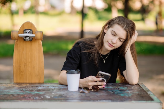 Portrait of pretty teenager girl with a skateboard is sitting and resting on the bench outdoors the skater park