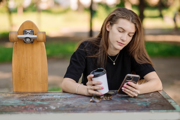 Portrait of pretty teenager girl with a skateboard is sitting and resting on the bench outdoors the skater park