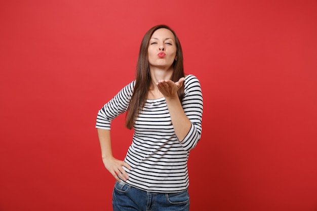 Portrait of pretty tender young woman in striped clothes standing, blowing kisses, send air kiss 