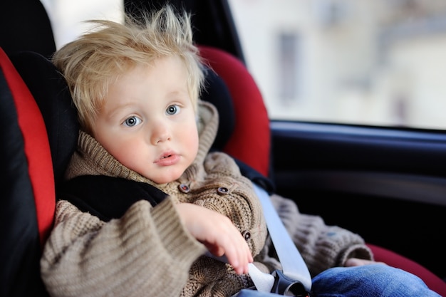 Portrait of pretty toddler boy sitting in car seat. Child transportation safety