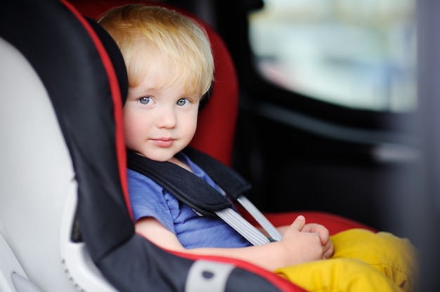 Portrait of pretty toddler boy sitting in car seat. Child transportation safety