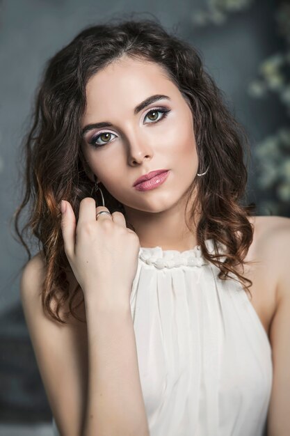 Portrait of a pretty woman bride with beautiful makeup in white dress on gray wall