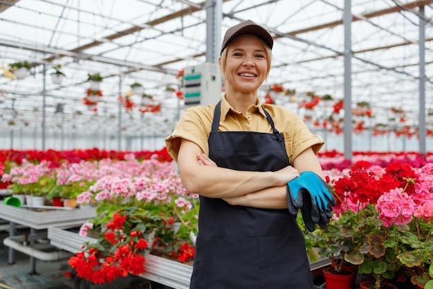 Portrait of pretty woman florist dressed in work uniform at the greenhouse