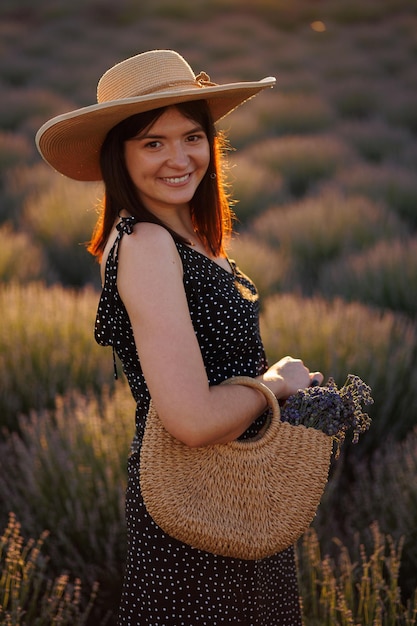 Portrait of a pretty woman in a straw hat and summer dress in a lavender field during sunset