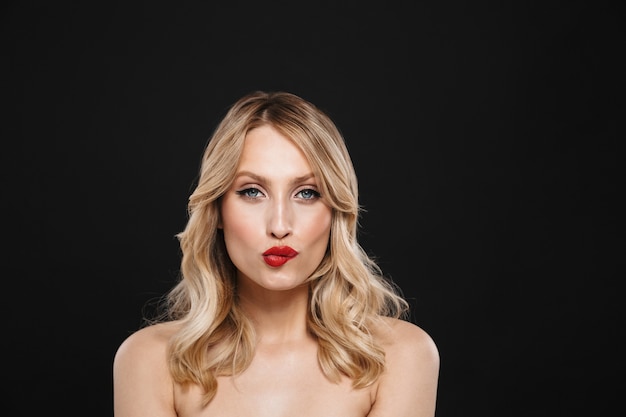 Portrait of a pretty young blonde woman with bright makeup red lips posing isolated bite her lip.