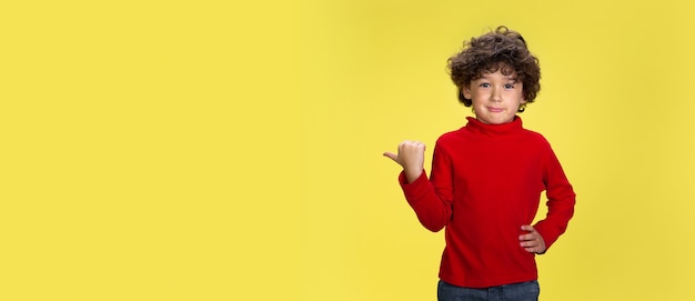 Portrait of pretty young curly boy in red wear on yellow  wall childhood expression