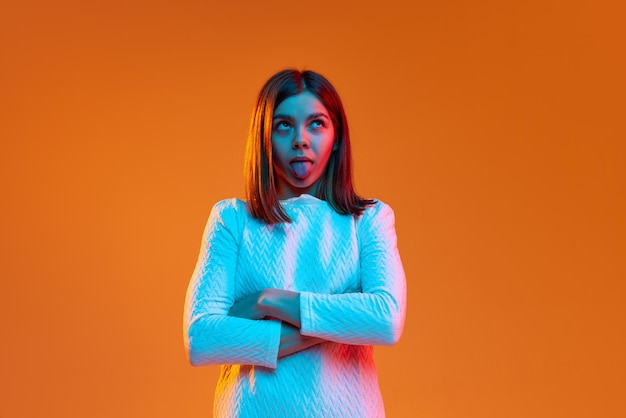 Portrait of pretty young girl looking posing with funny grimacing face against orange studio