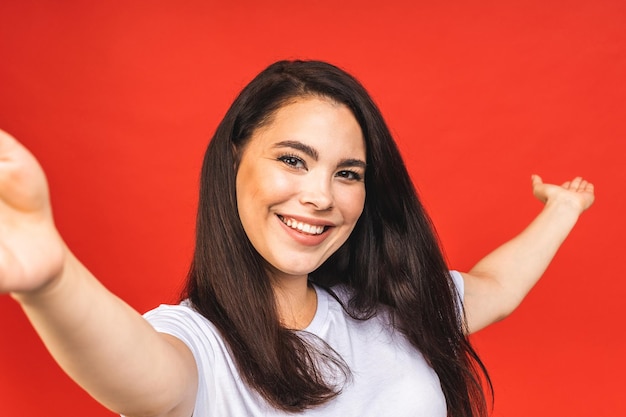 Portrait of pretty young happy woman making selfie on smartphone isolated over red background