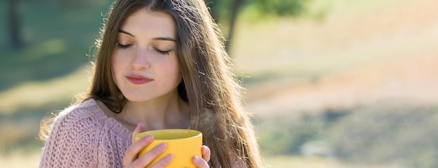 Portrait of pretty young woman in stylish knitted sweater standing on the golden autumn forest on sunny day