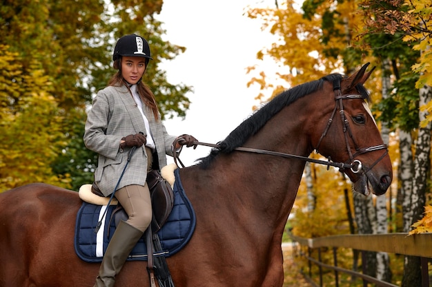 Portrait of a pretty young woman with a brown horse riding autumn day