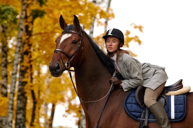 Portrait of a pretty young woman with a brown horse riding autumn day