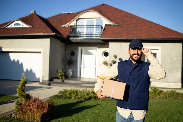 Portrait of professional delivery man standing in front of the house and delivering packages