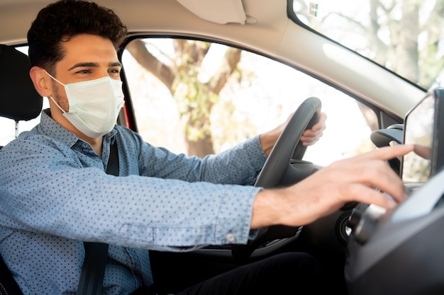 Portrait of professional male driver wearing face mask and using gps navigation system in car.Transport  concept. New normal lifestyle concept.