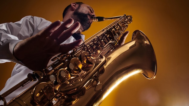 Portrait of professional musician saxophonist man in  white shirt plays jazz music on saxophone, yellow background in a photo studio, bottom view