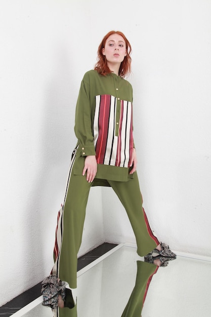 Photo portrait of red hair woman standing on big mirror in simple interior with white walls fashion