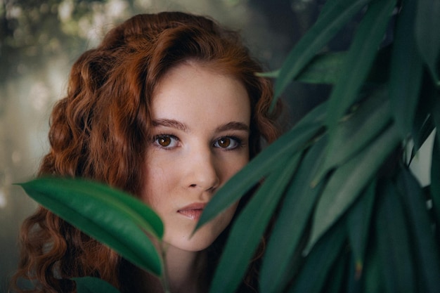 Portrait of a red-haired teenage girl with curly hair on a background of green plants