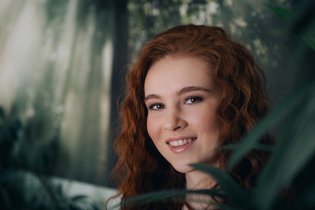 Portrait of a red-haired teenage girl with curly hair on a background of green plants