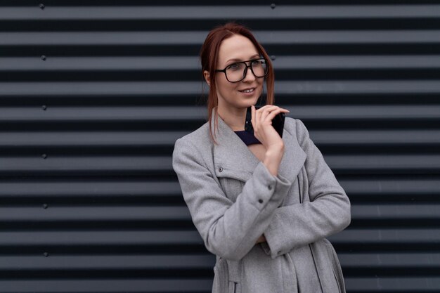 Portrait of a redhaired business woman in eyeglasses against a gray wall business insurance concept