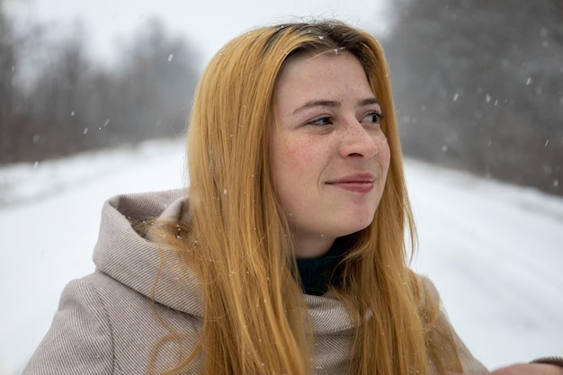 Portrait of a redhaired girl with freckles on her face With blurred snow background